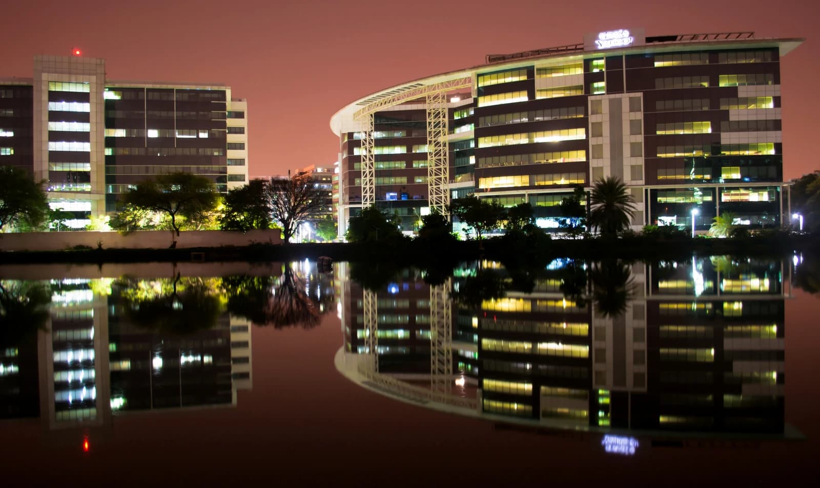 Buildings of Bhagmane Tech Park illuminated at night with reflections in water.