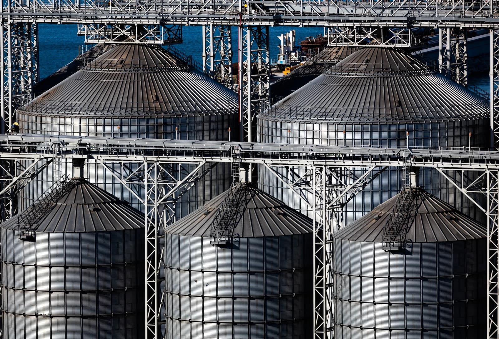 Multiple large grain silos at the KSK terminal near a body of water.