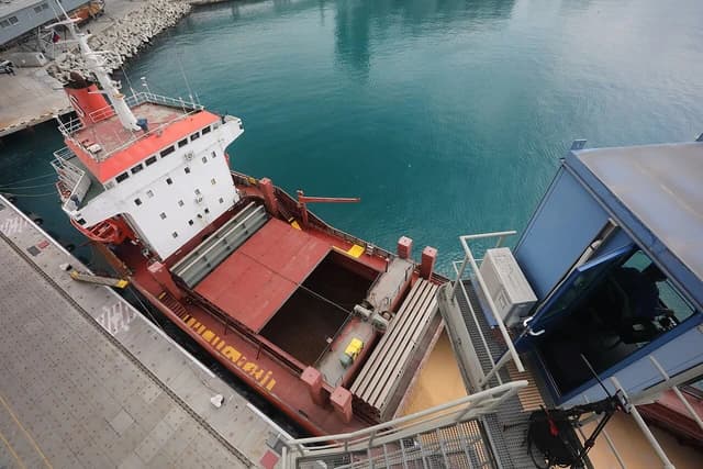Grain being loaded into the hold of a large cargo ship at a port terminal.
