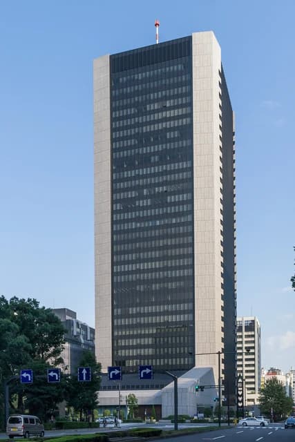 Mizuho Bank Headquarters building, a tall modern skyscraper, stands against a clear blue sky.