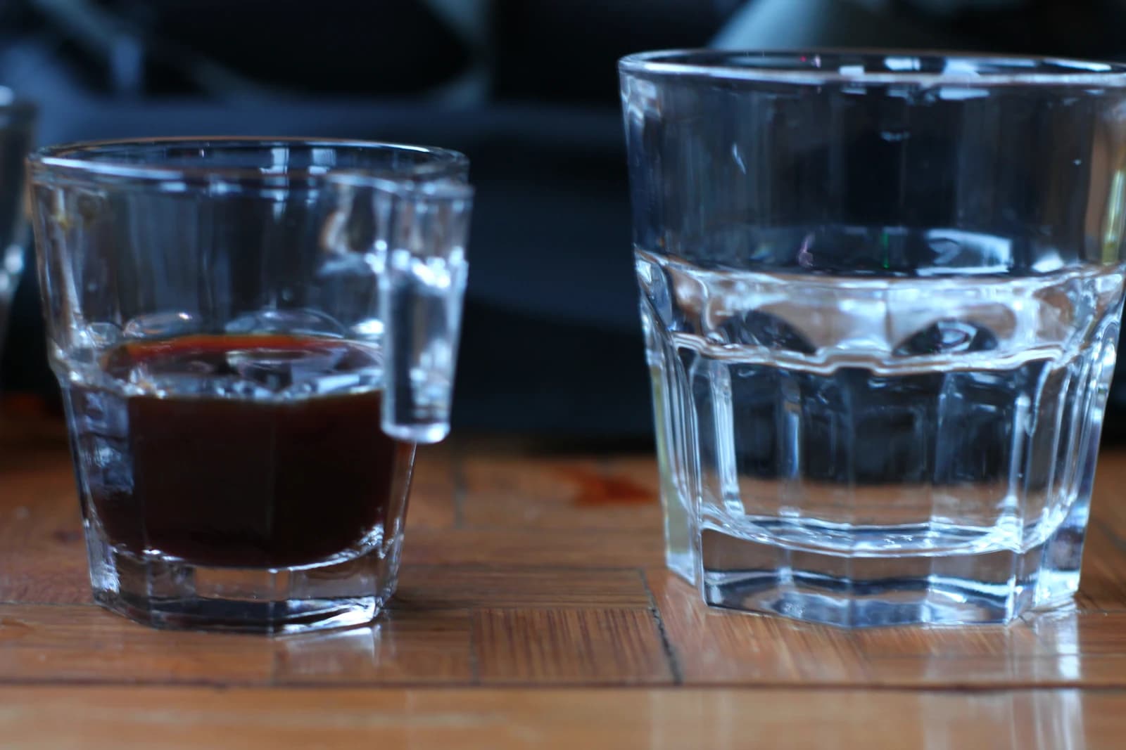 A small glass of black coffee beside a clear glass of water on a wooden surface.