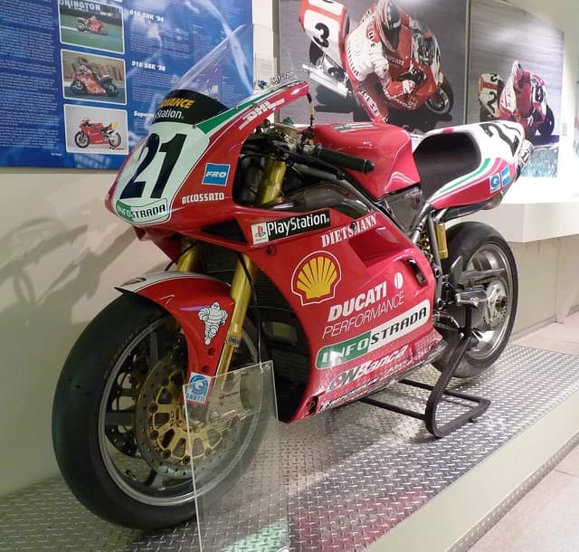 Red Ducati 996 motorcycle on display at a museum with race numbers.