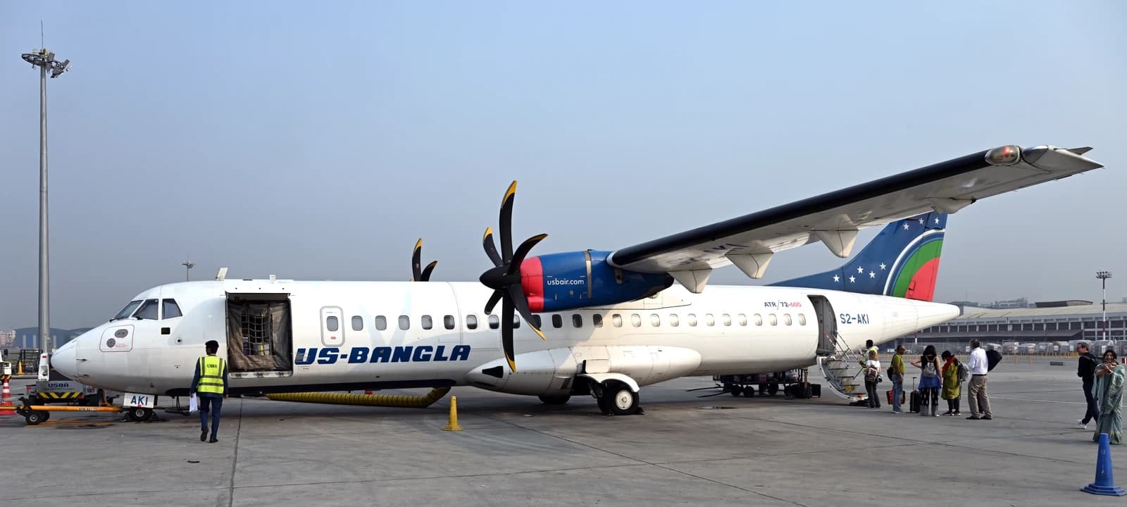 US-Bangla Airlines aircraft on tarmac at Dhaka airport with passengers boarding.
