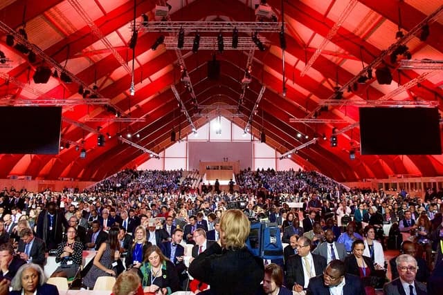 Delegates gather in a large hall with a red and white ceiling during a climate change conference.