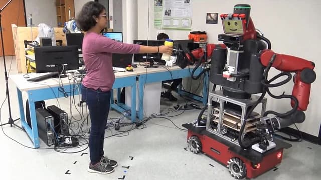 Researcher handing an object to a Baxter robot in a laboratory.