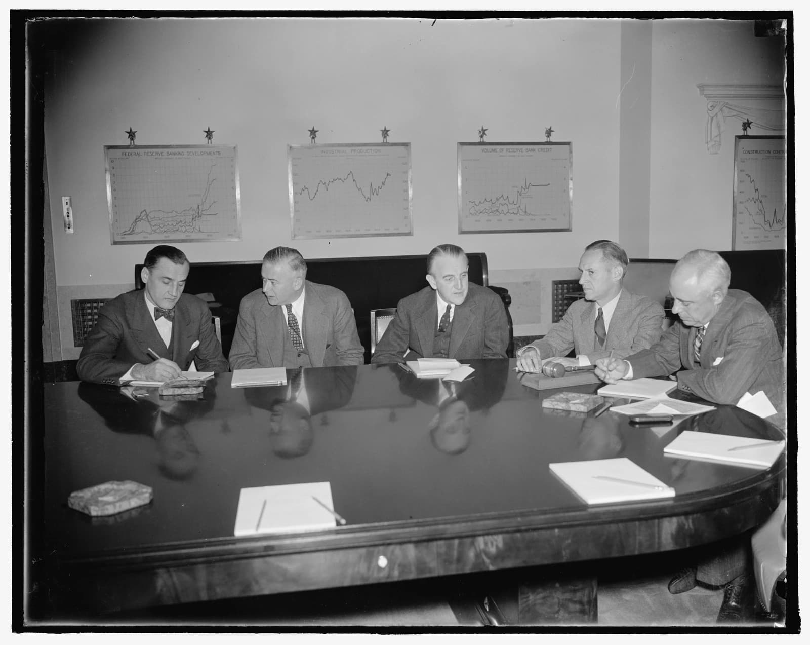 Federal Reserve System board members in suits, seated around a large meeting table.