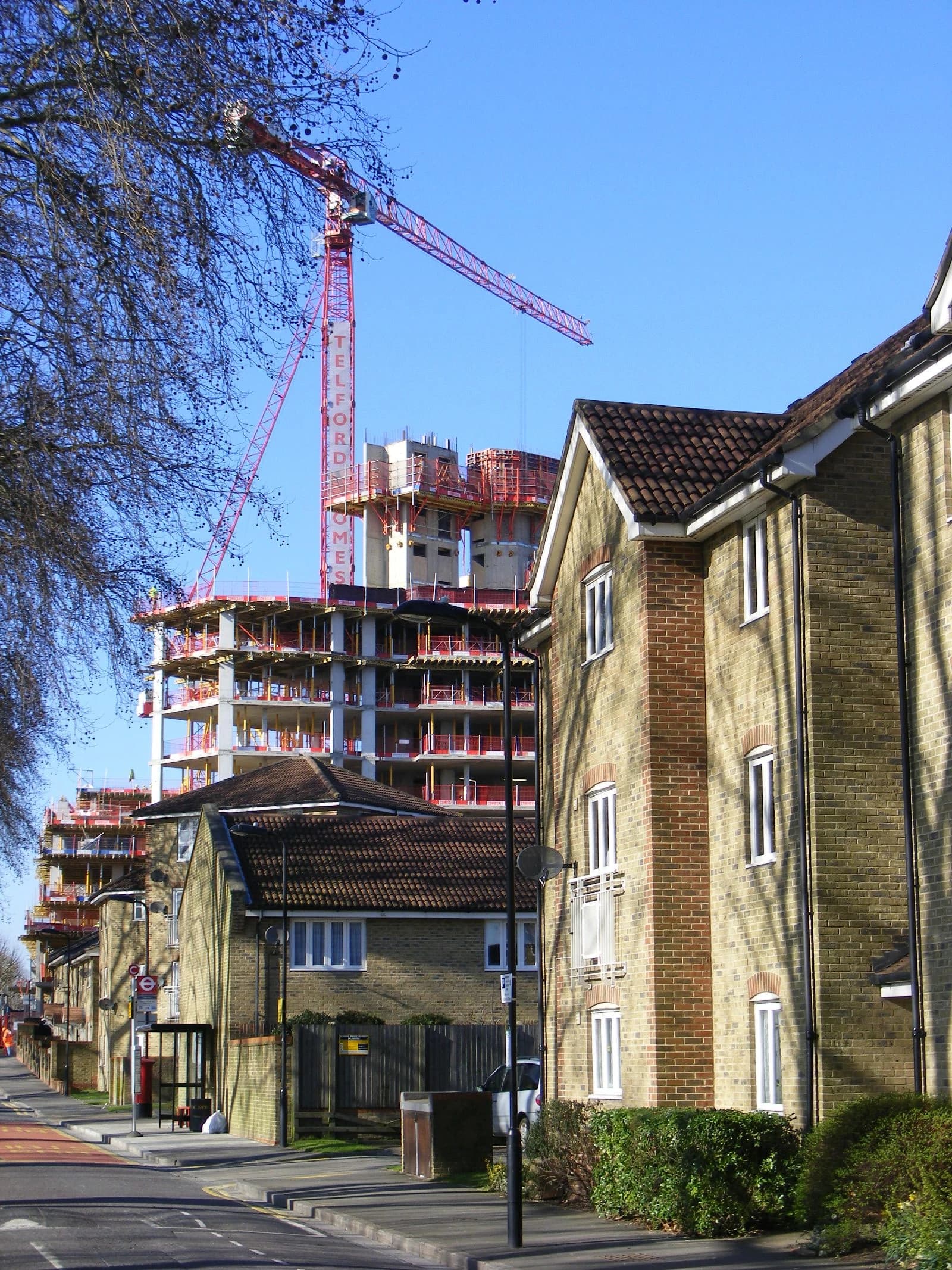 A large red construction crane towering over apartment buildings and older residential properties.