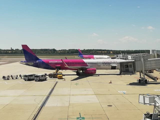 Two Wizz Air passenger airplanes parked at an airport gate on a sunny day.
