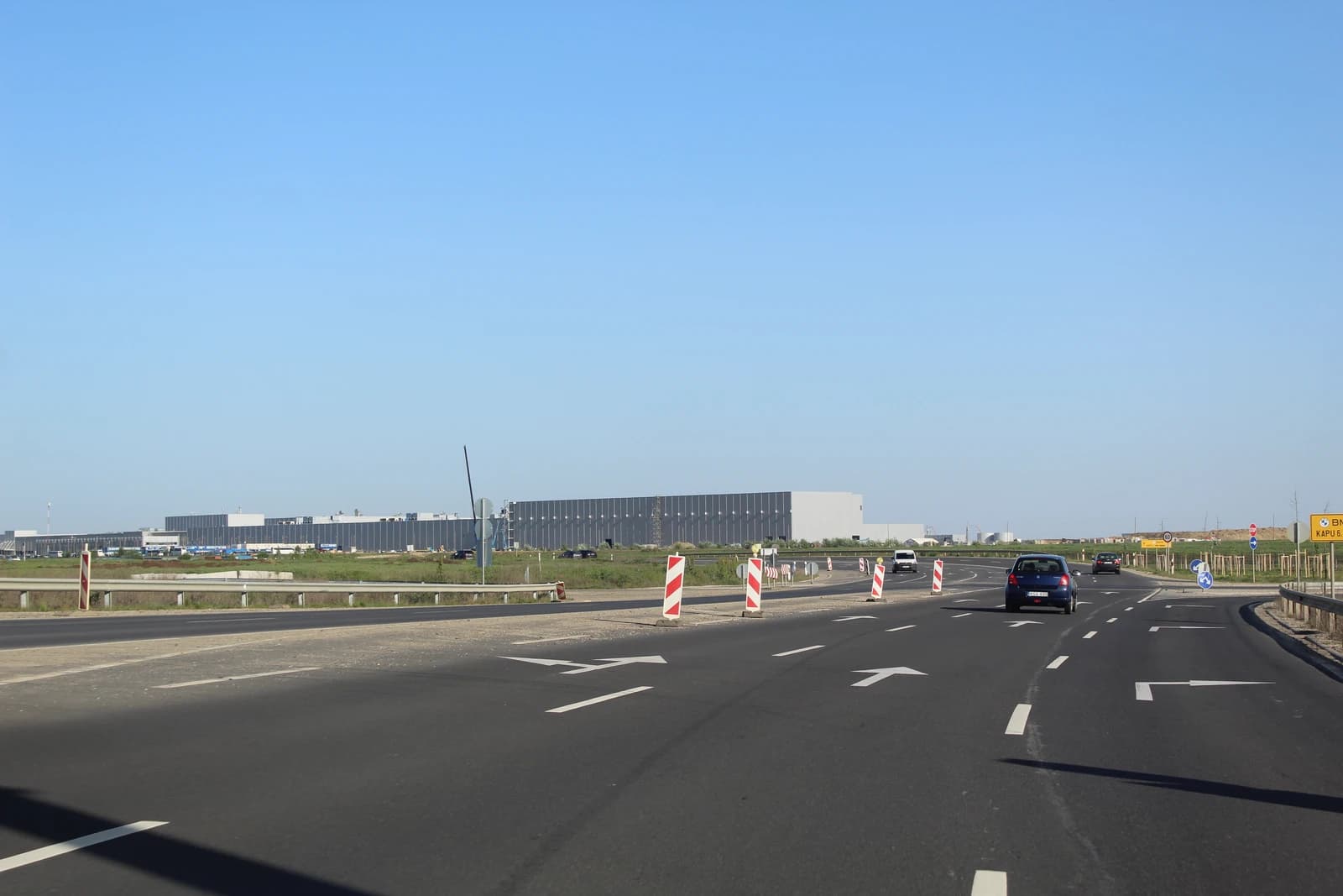 Road with cars leading towards a large industrial building, the BMW factory in Debrecen.