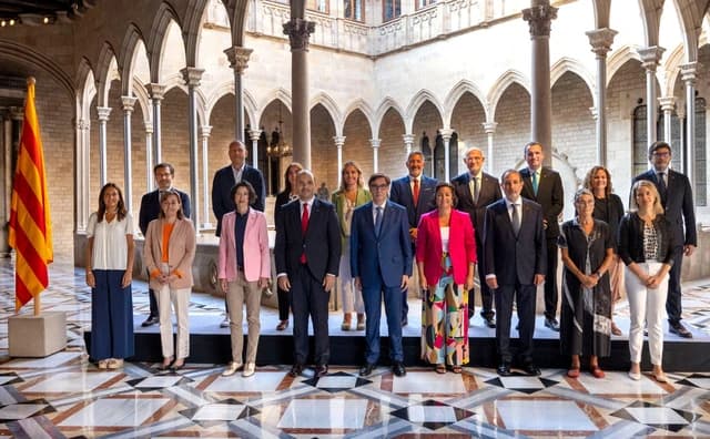 Group of political figures posing for a photograph in a historic courtyard with a Catalan flag.