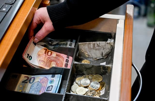 Person's hand placing Euro banknotes into a cash register drawer.