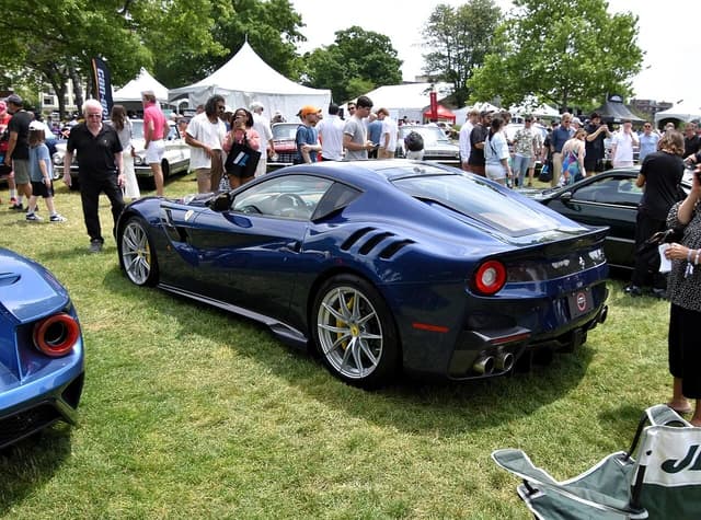 Blue Ferrari F12tdf luxury sports car parked on green grass at an outdoor car show.