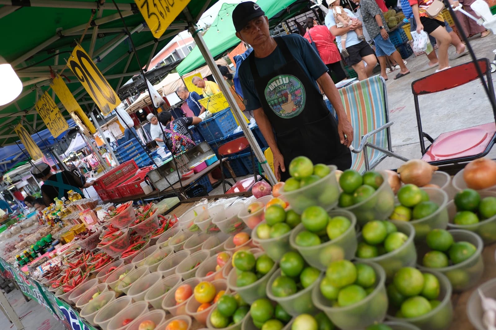 A vendor standing behind a market stall with bowls of limes and other produce.