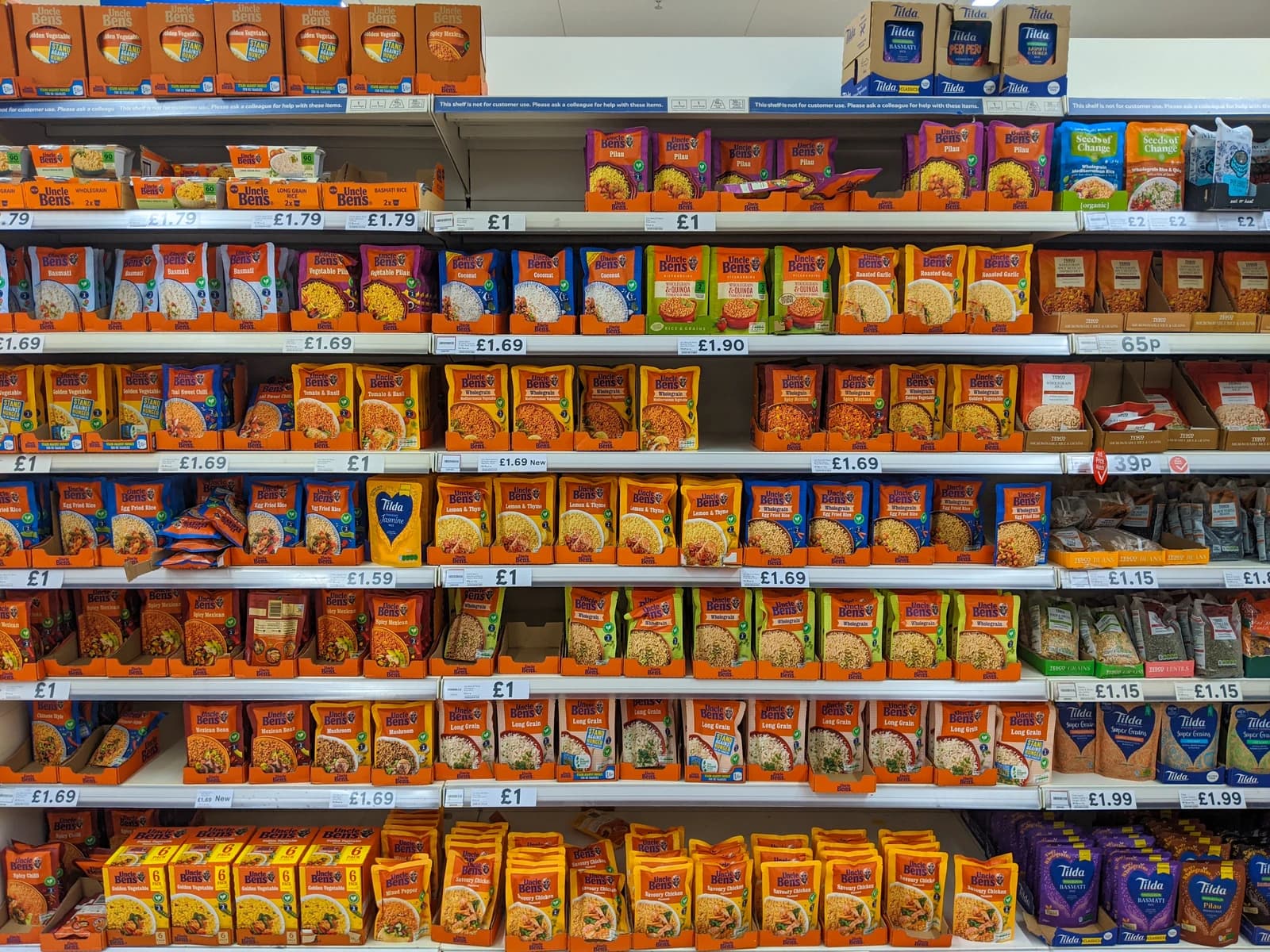 Supermarket aisle displaying numerous packages of rice, including Uncle Ben's and Tilda brands.