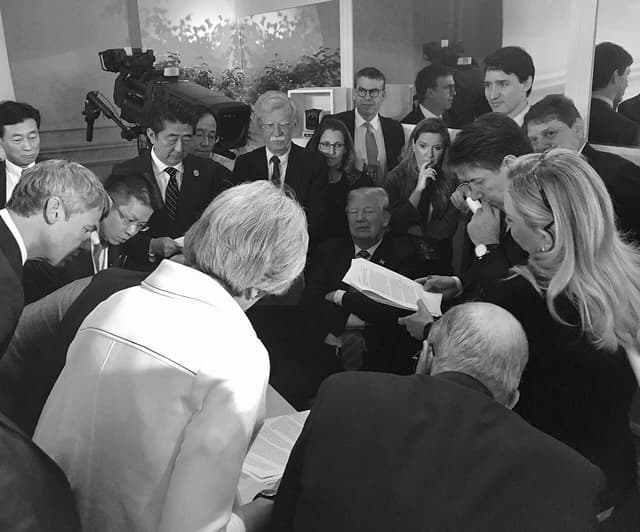 President Donald Trump sits at a table surrounded by world leaders reviewing documents.