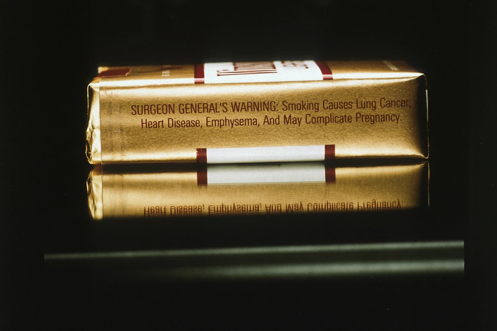 Side view of a gold-colored cigarette pack on a reflective surface.