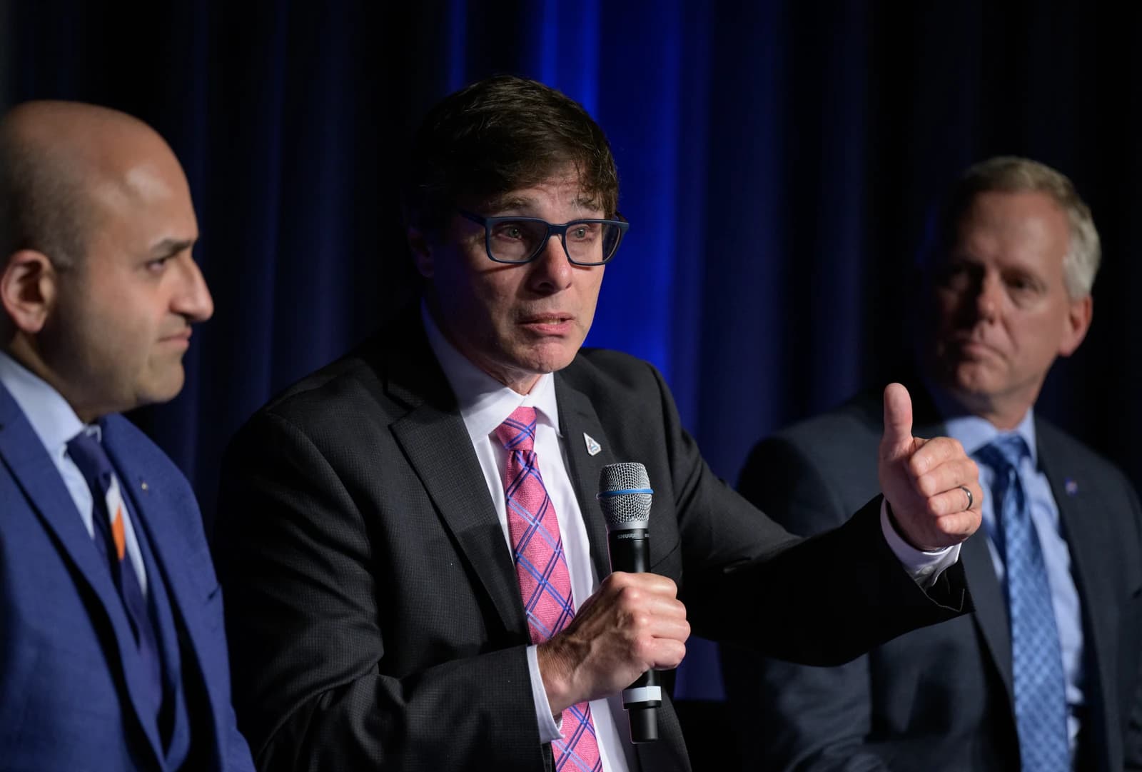 Man in glasses and suit speaking into a microphone at an event.