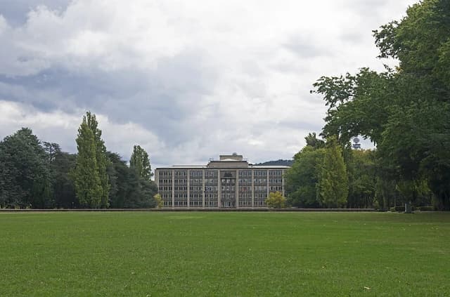 The Treasury Building in Canberra, Australia, stands behind a green lawn under a cloudy sky.