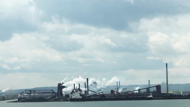 Steel mill in Hamilton, Ontario, with industrial structures, smoke stacks, and cargo on the water.