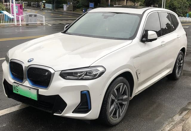 White BMW iX3 vehicle parked on a wet city street.