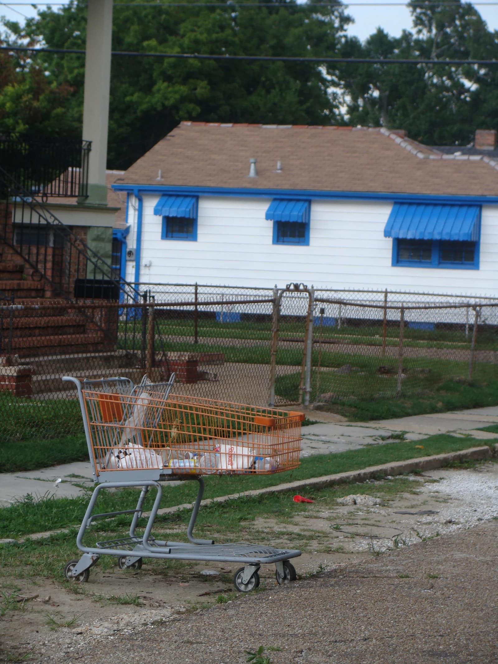 Abandoned shopping cart filled with plastic bottles and debris on a sidewalk.
