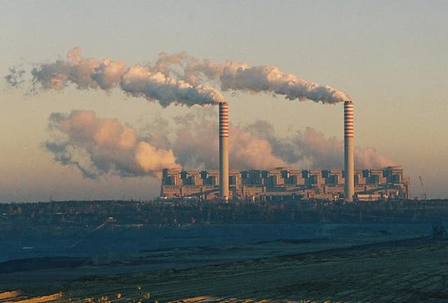 Bełchatów Power Station with multiple cooling towers emitting large plumes of smoke into the sky.