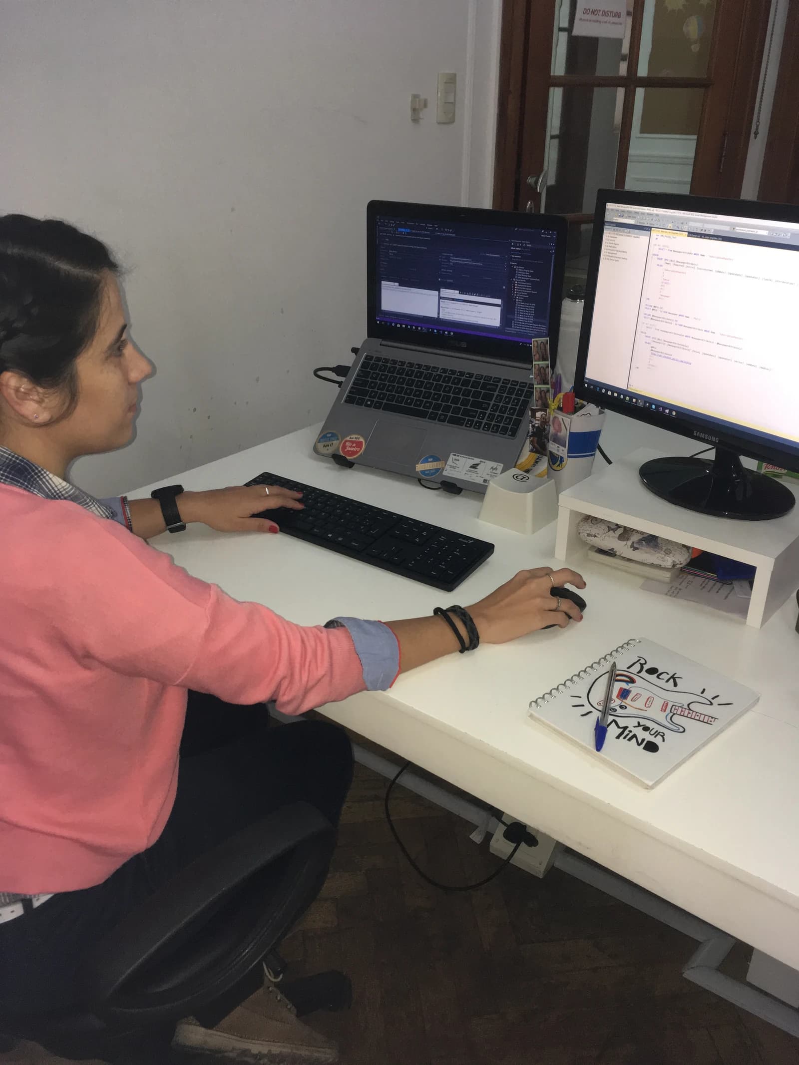 Woman working at a desk with two computer monitors displaying code.