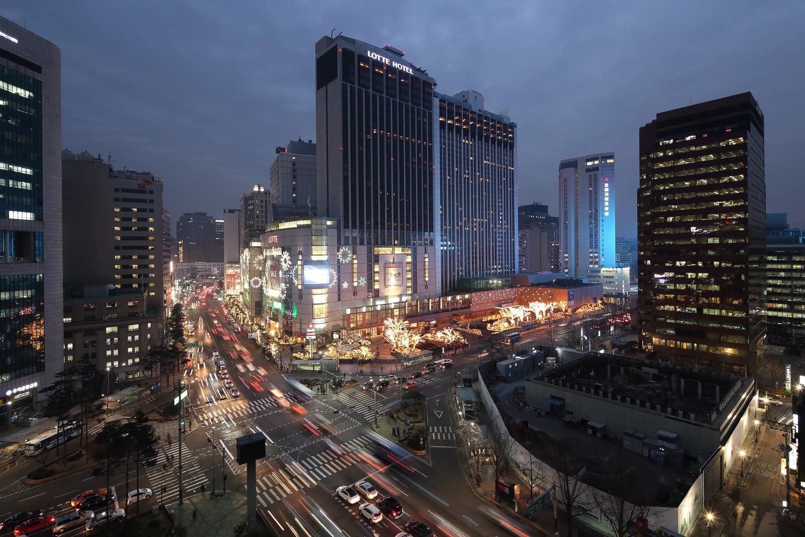 Night view of a bustling intersection with tall buildings and moving cars in Seoul.