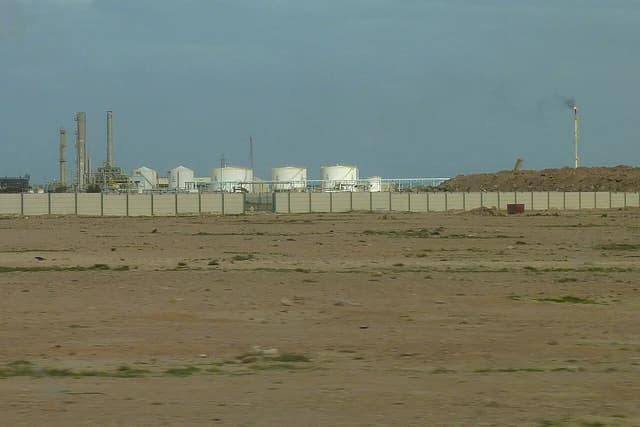 An oil refinery with multiple storage tanks and industrial structures behind a fence.