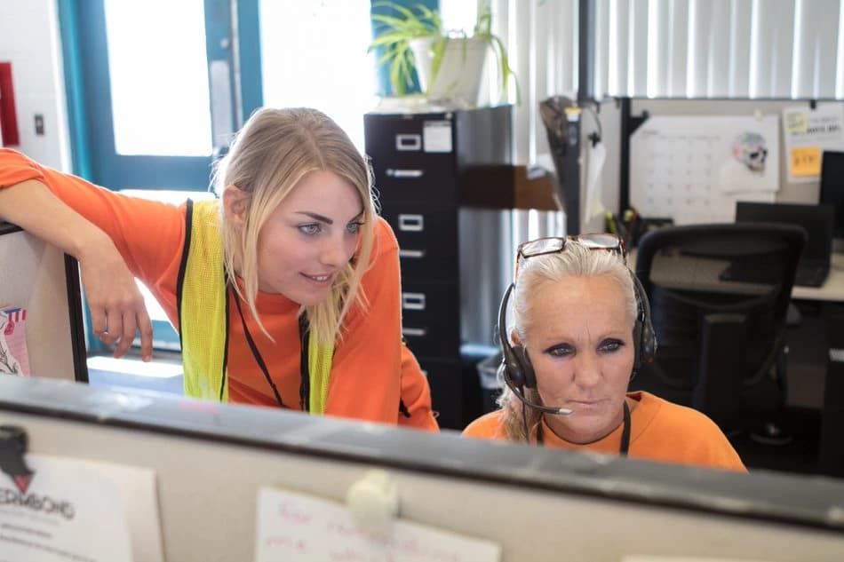 Two women, one with blonde hair, the other with gray hair, in a call center.