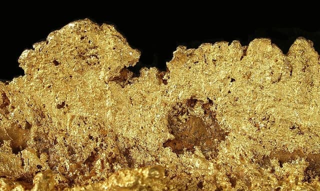 Close-up of a large, irregularly shaped raw gold nugget on a black background.