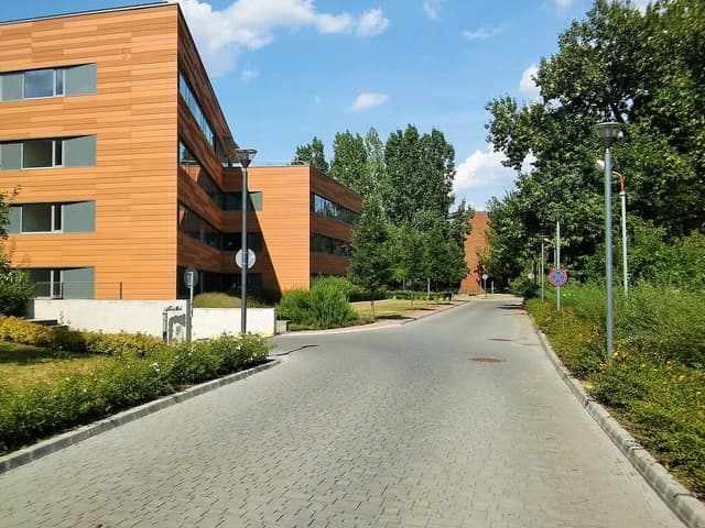 Modern office buildings with brown paneling line a paved road in Óbuda, Hungary.