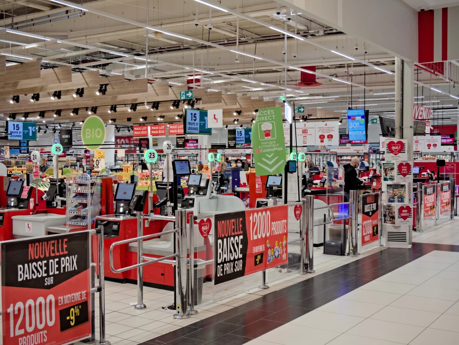 Supermarket interior with self-checkout counters and signs advertising price drops on products.