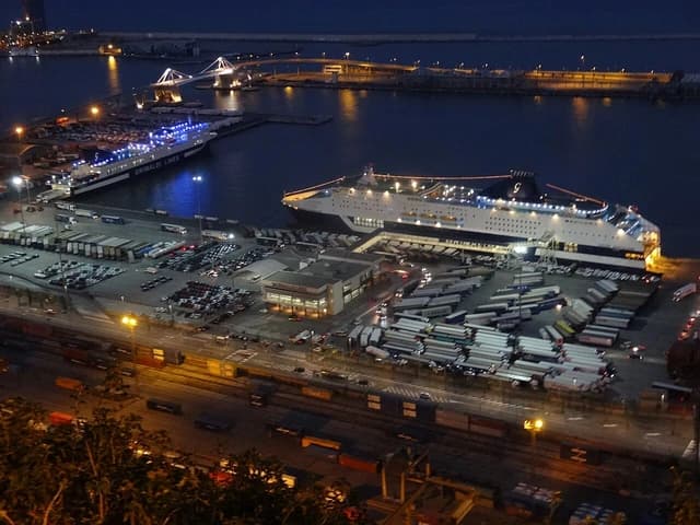 Aerial view of Grimaldi Lines terminal in Barcelona at night with multiple large ships docked.