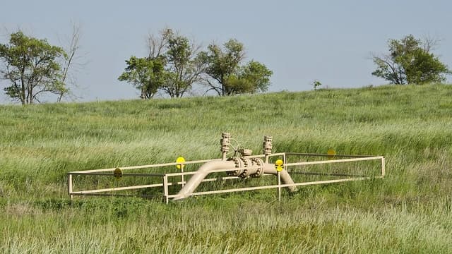 Above-ground gas pipeline valve with a protective fence in a field of tall grass.