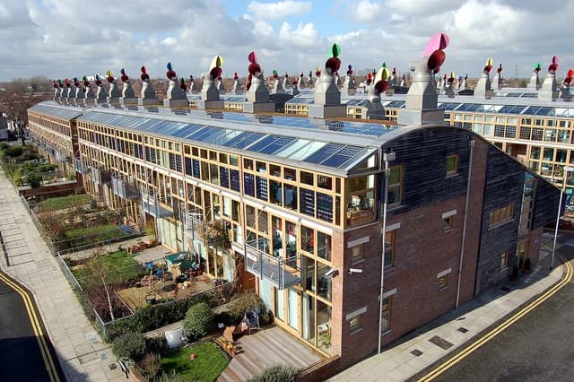 Aerial view of BedZED buildings with numerous solar panels and distinctive wind cowls on roofs.
