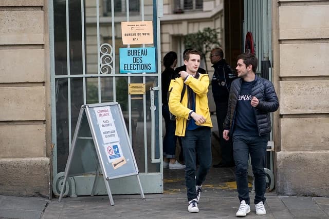 Two men exit a polling station labeled "Bureau des Elections" in Paris.