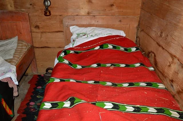 A rustic wooden bed with a red, green, and white patterned blanket in an old room.