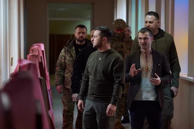 Volodymyr Zelenskyy, President of Ukraine, standing indoors with other men.