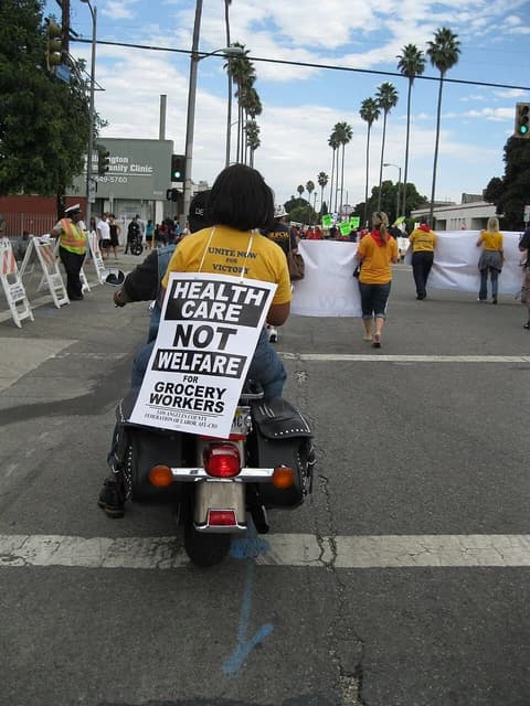 Healthcare worker riding a motorcycle with a sign advocating for healthcare.
