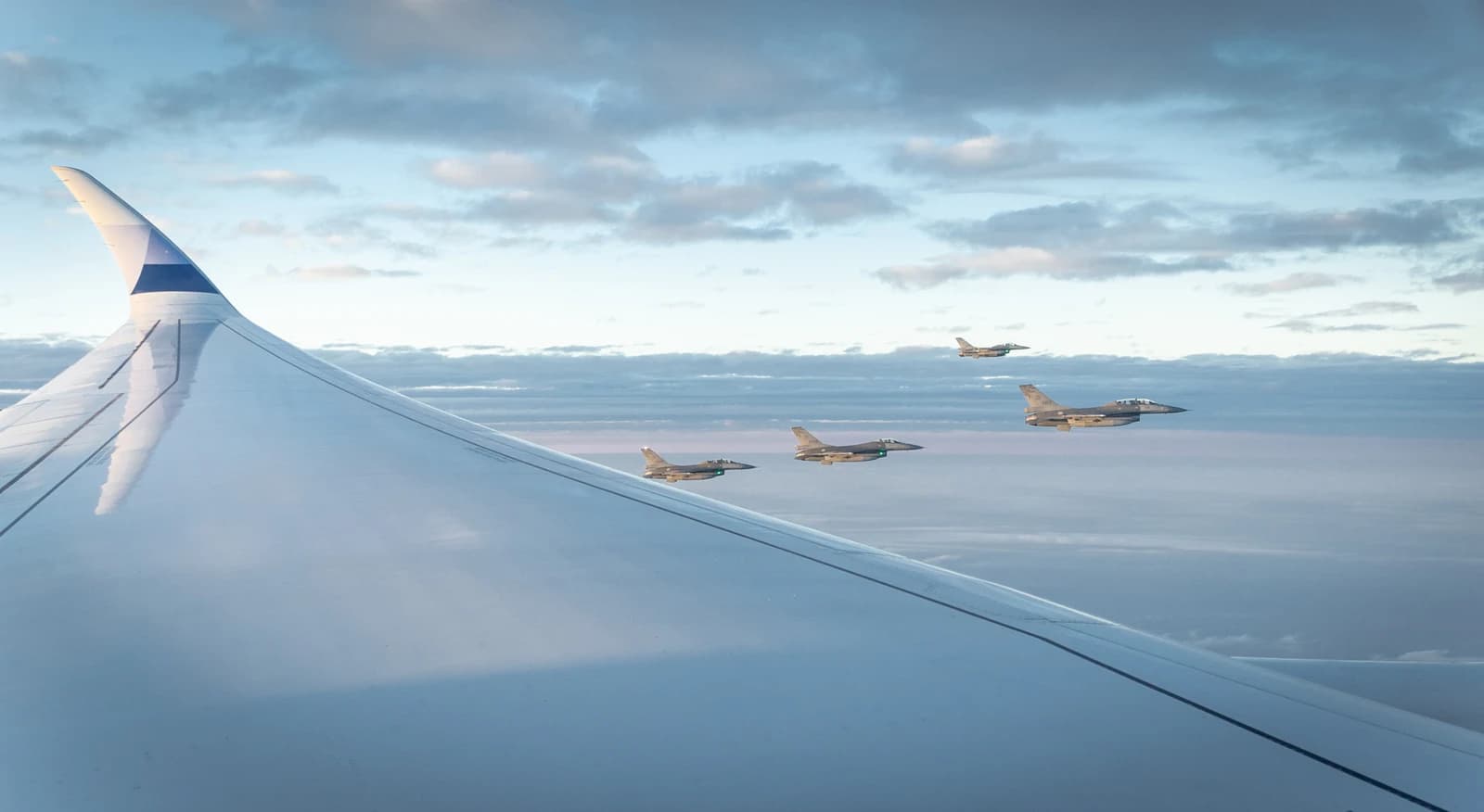 Four F-16V fighter jets flying in formation alongside an airplane wing.