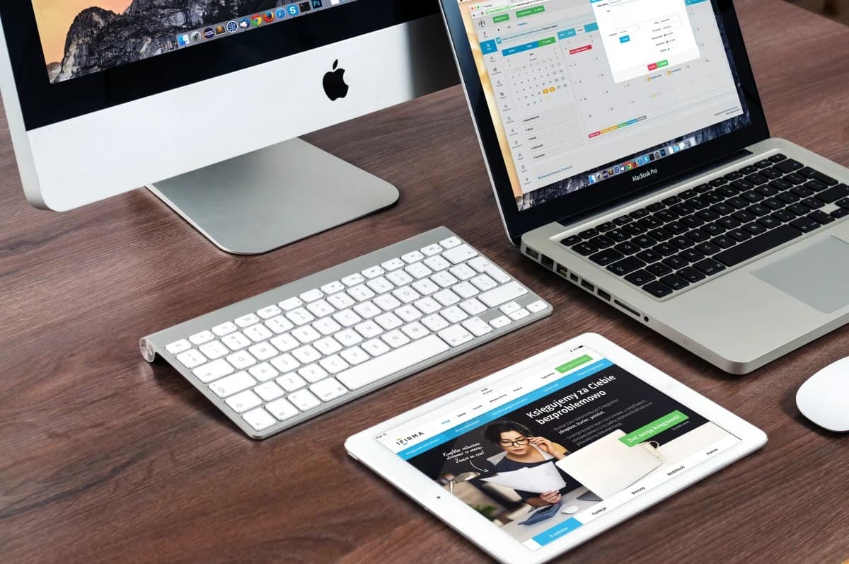 An Apple iMac, MacBook Pro, and iPad are shown on a wooden desk.