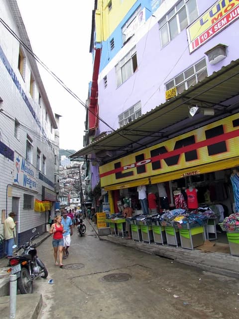 People walking on a narrow street between buildings in Riocinha Favela, Rio de Janeiro.