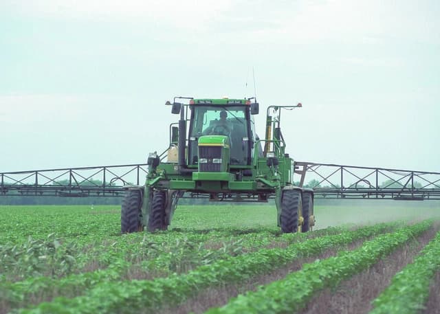 Farmer operating a green sprayer vehicle in a cultivated field.
