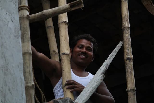 Male laborer holding bamboo scaffolding at a building construction site in India.