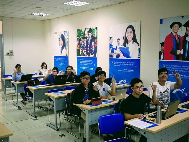 Vietnamese students in a classroom with laptops, some making peace signs for the camera.