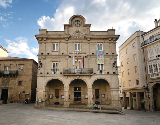 Exterior view of the Concello de Ourense building with a clock tower and flags.