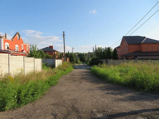 A damaged orange house with a broken roof stands next to a dirt road in Tsyrkuny.