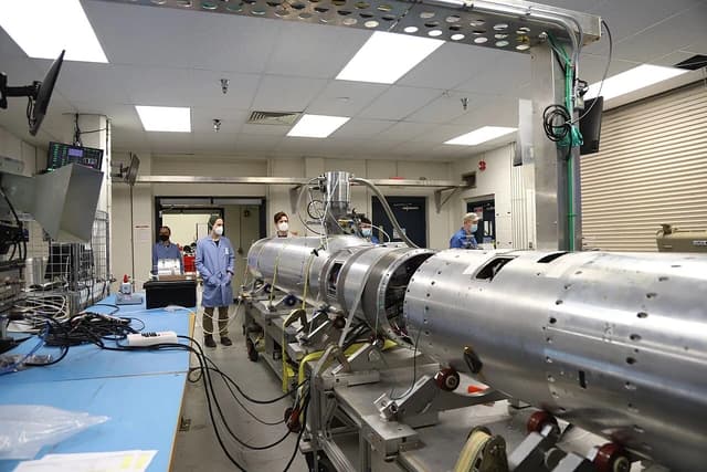 Engineers in a clean room facility working on a large, cylindrical piece of rocket hardware.