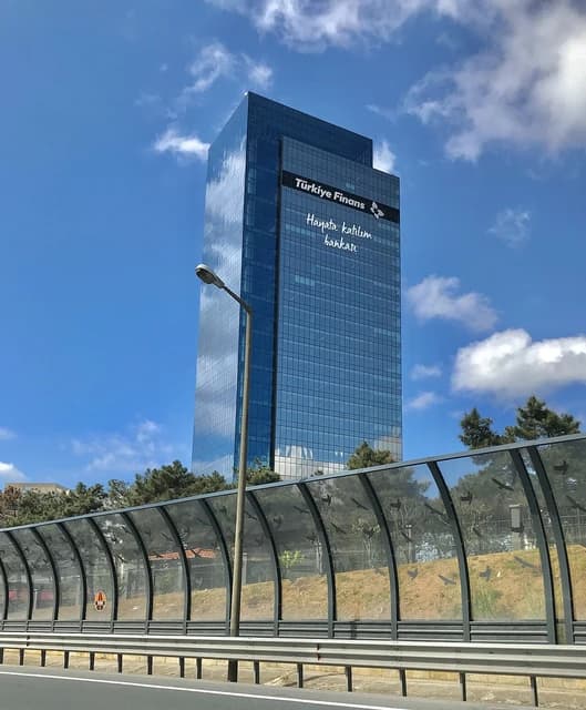 Modern glass skyscraper with 'Türkiye Finans' logo and text on its facade.